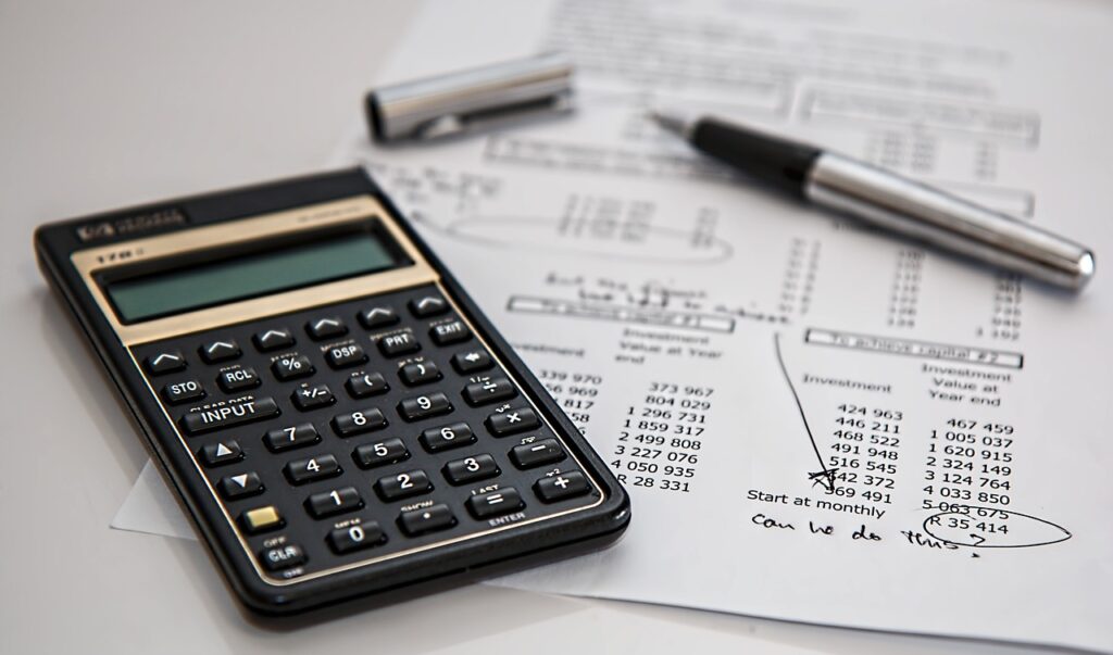 A black calculator and under it a pen and paper with a financial computation, where there's a scribble under saying, "Can we do this?"