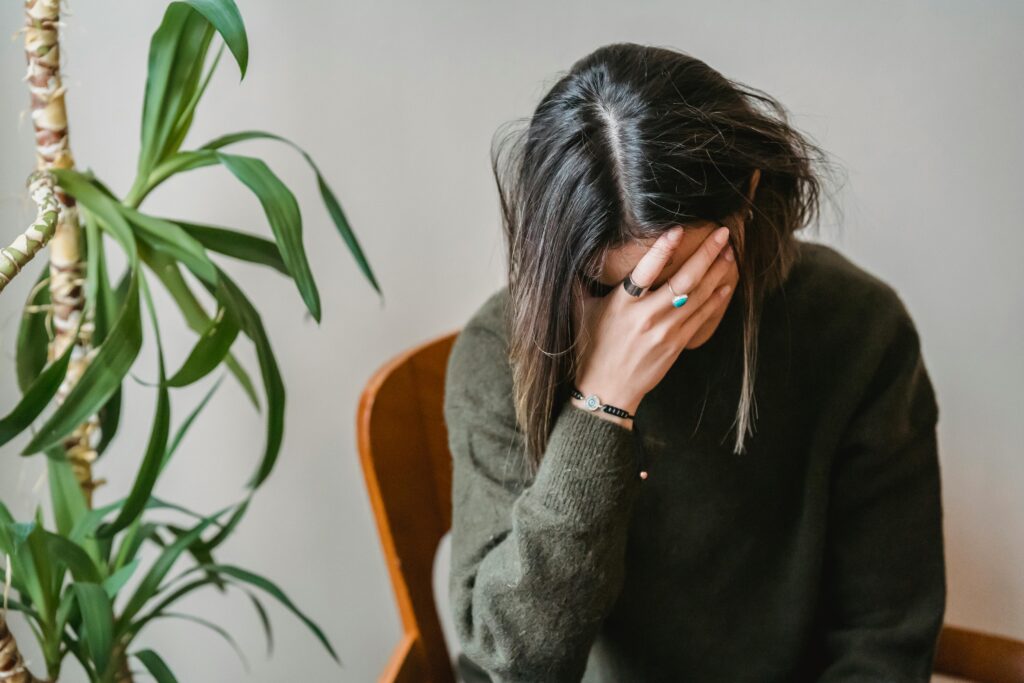 A woman sitting in a chair with her hand covering her face, visibly worried.